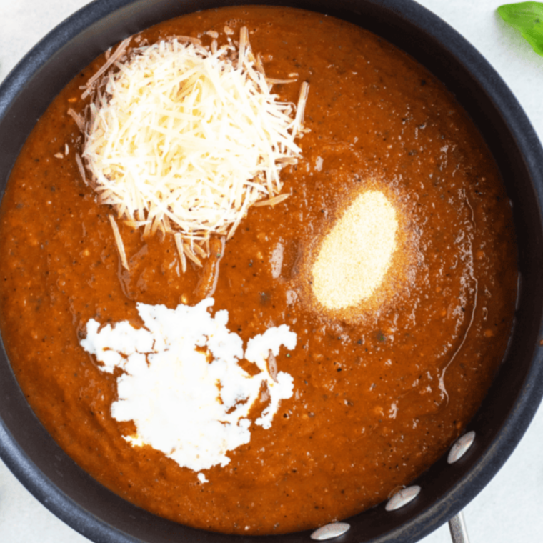Whole milk being whisked into browned tomato soup concentrate in a saucepan on the stove.