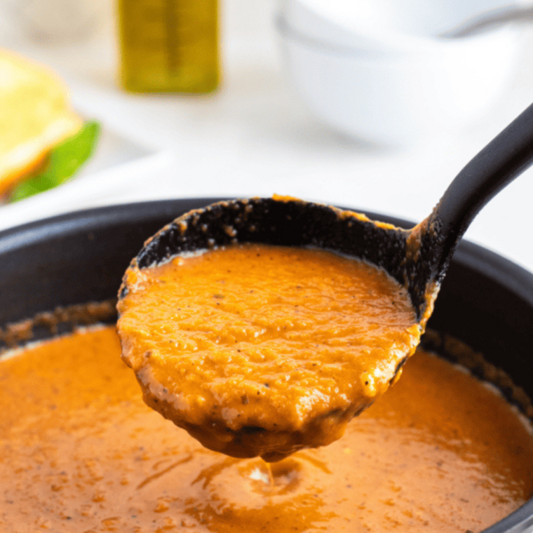 Close-up of thick, creamy tomato soup with melted Parmesan and cracked black pepper on the surface.