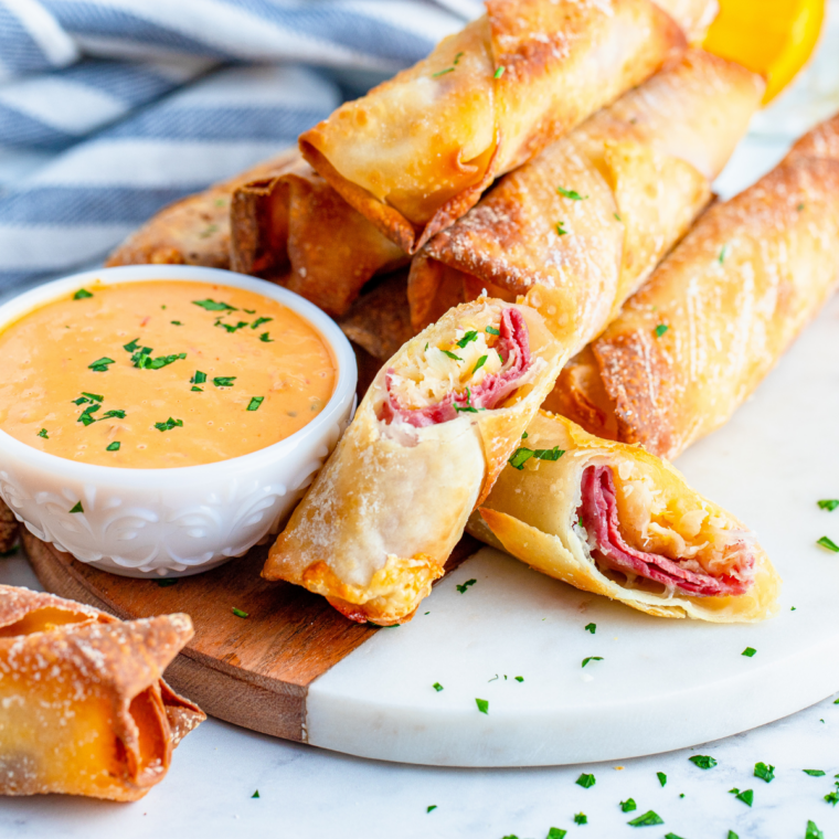 Crispy egg rolls being dipped into a bowl of copycat Ken's Boom Boom Sauce