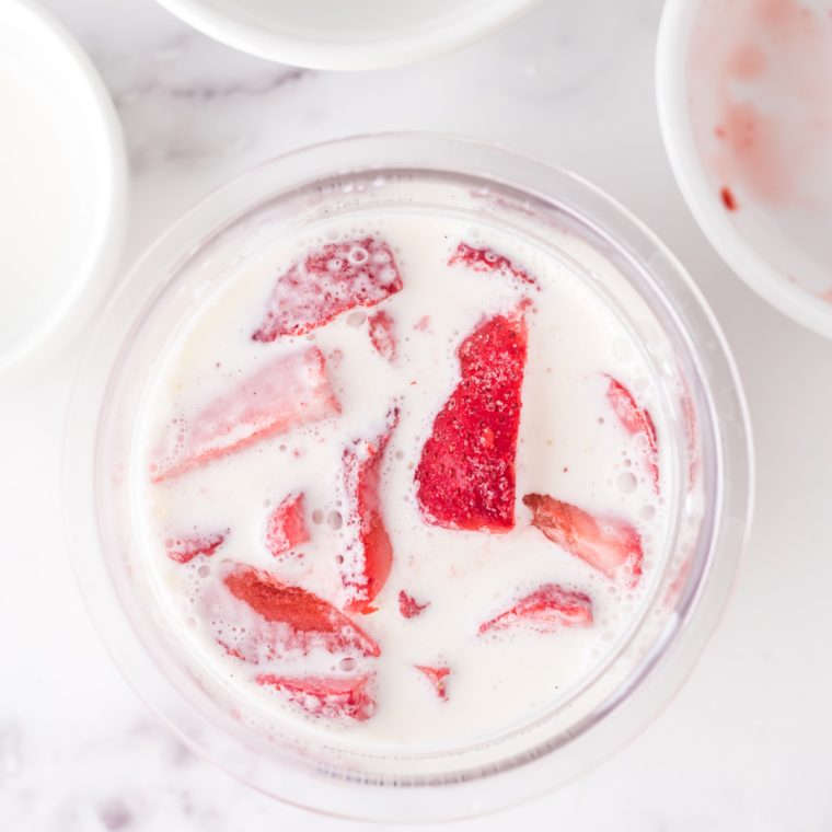 Pouring pink strawberry ice cream base into a Ninja Creami pint container to the MAX FILL line