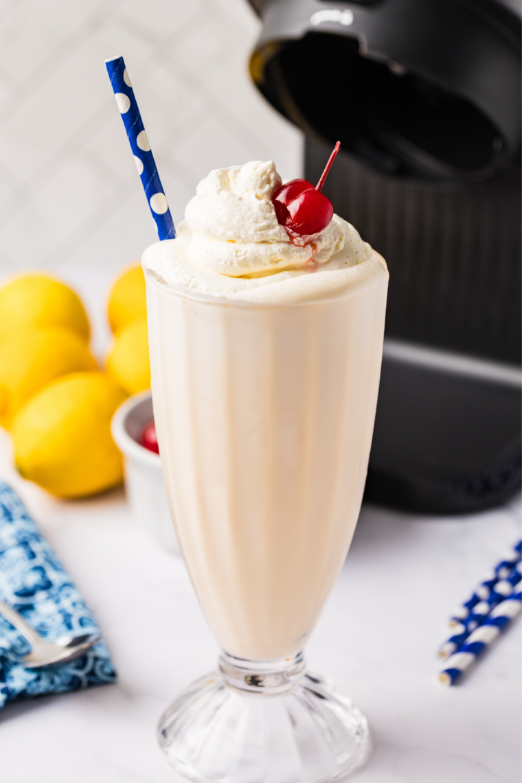 Finished Ninja Creami Frosted Lemonade milkshake poured into a glass with whipped cream and lemon