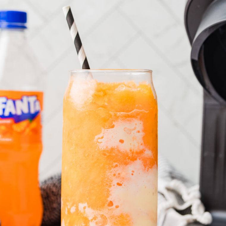 Ninja Creami Fanta Float Slushie in a tall glass topped with a scoop of vanilla ice cream, straw, and spoon