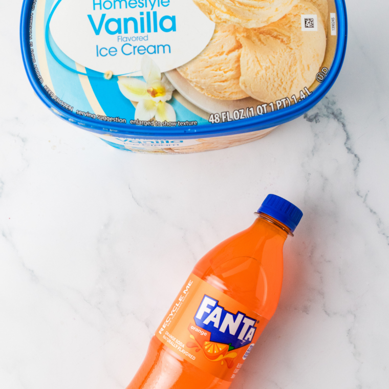 Ingredients for a Ninja Creami Fanta float: a bottle of orange Fanta, water, and vanilla ice cream on a counter