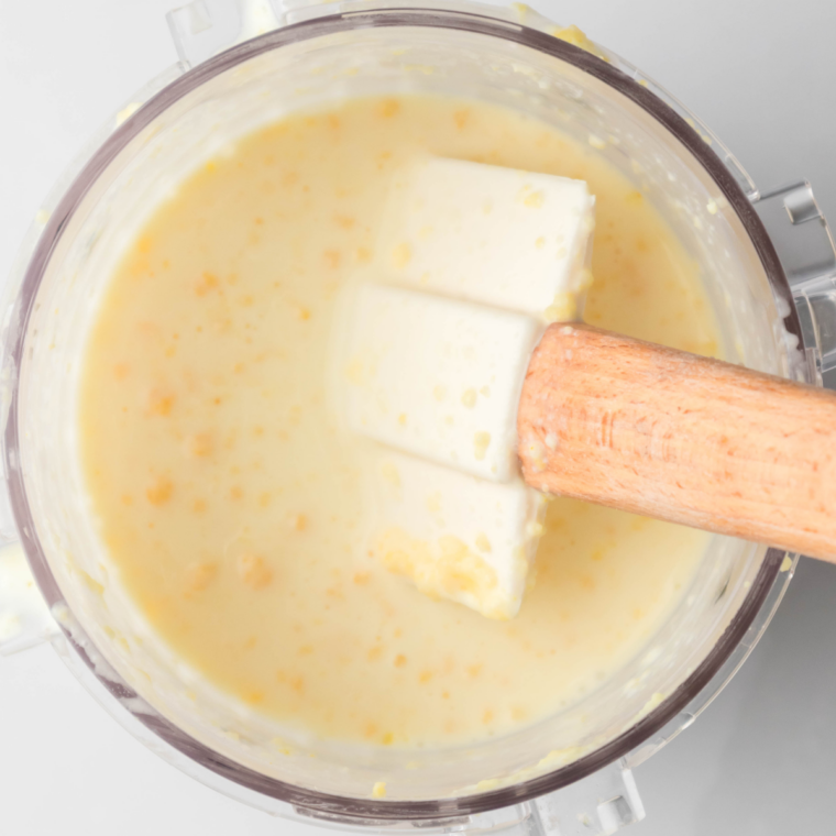 Peanut butter ice cream base being blended smooth in a Ninja Creami pint with an immersion blender.