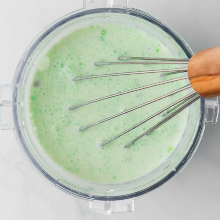 Pouring pale green pistachio base into a Ninja Creami pint container