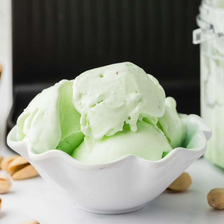 Two scoops of homemade Ninja Creami pistachio ice cream in a white bowl with toasted pistachios