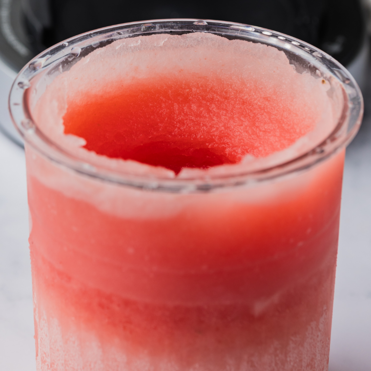 Vibrant pink Ninja Creami watermelon Italian ice in a waffle cone against a bright summer backdrop