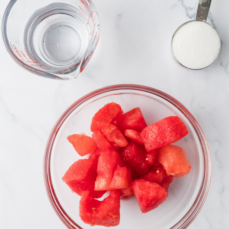 Ingredients for Ninja Creami watermelon Italian ice: fresh watermelon chunks, sugar, water, and lime on a countertop