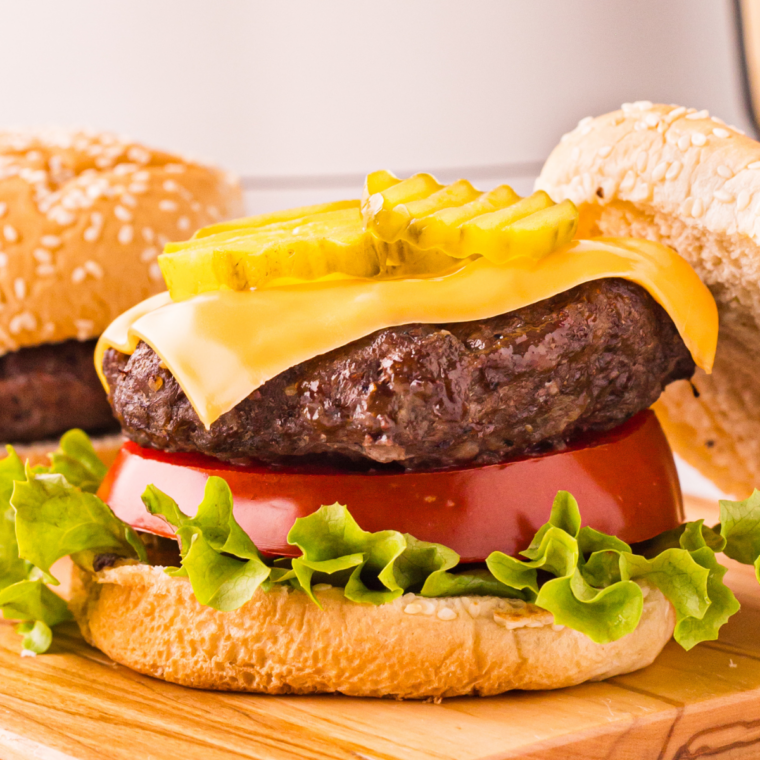 Two juicy cheeseburgers with melted American cheese on toasted buns beside the Ninja Crispi