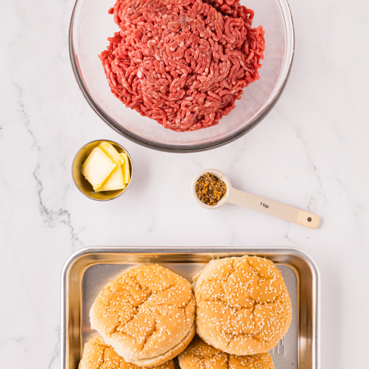 Ground beef, kosher salt, black pepper, cheese slices, and burger buns arranged on a marble counter