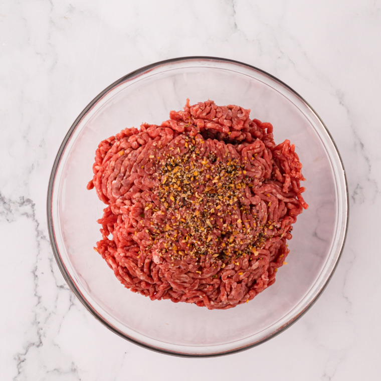 Ground beef and seasonings in a glass mixing bowl before shaping into patties