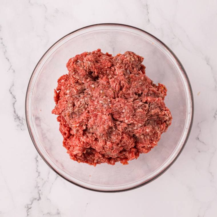 Ground beef combined with salt, pepper, and garlic powder in a clear glass bowl