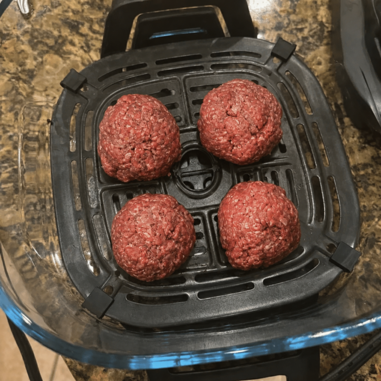 Four raw burger patties in a single layer on the crisper plate in the 4-quart container
