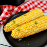 Ninja Crispi corn on the cob with melted butter and charred kernels on a white plate
