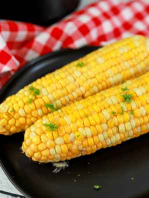 Ninja Crispi corn on the cob with melted butter and charred kernels on a white plate