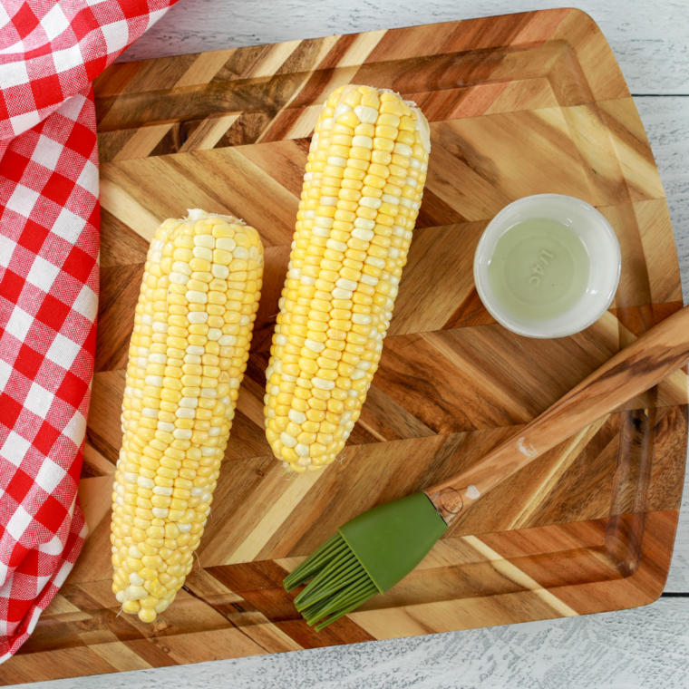 Ears of corn cut in half crosswise on a cutting board next to a chef's knife