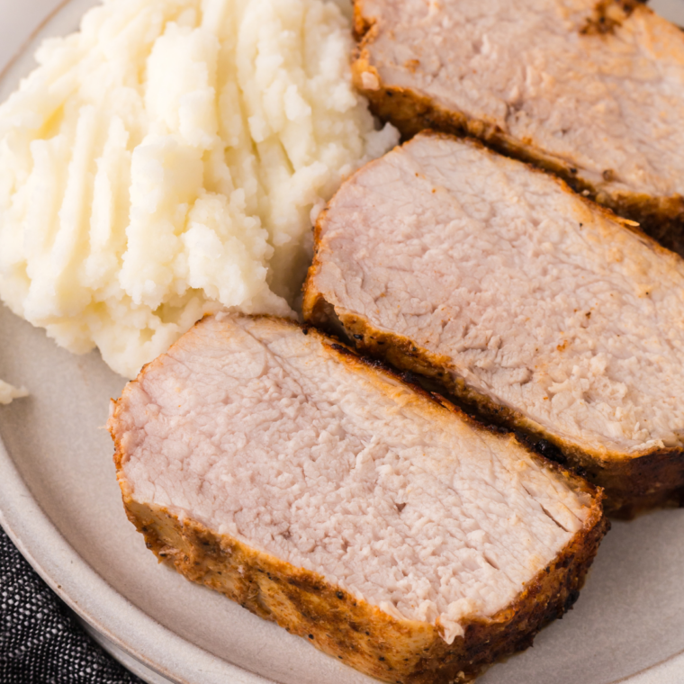 Sliced Ninja Crispi pork tenderloin with a golden crust served over mashed potatoes on a white plate