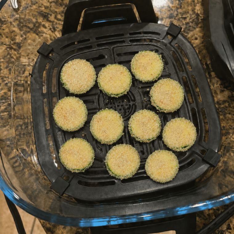 Breaded zucchini rounds arranged in a single layer on the Ninja Crispi crisper plate