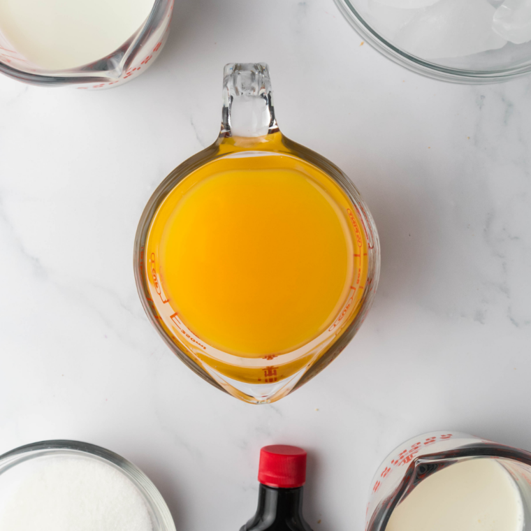 Ingredients for a Ninja Slushi Orange Julius laid out: orange juice, milk, sugar, and vanilla extract