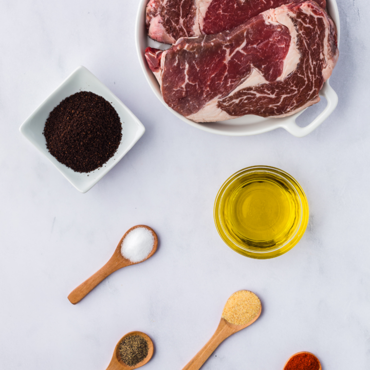 Ingredients for Outlaw Ribeye laid out, including a bone-in ribeye steak, seasoning spices, butter, and garlic