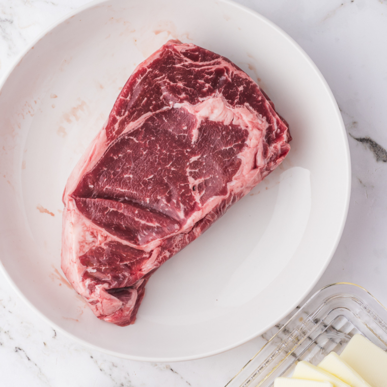 Raw bone-in Outlaw Ribeye resting at room temperature and patted dry on a cutting board before cooking