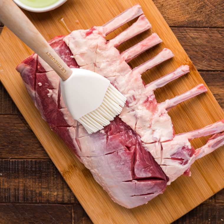 Lamb chops marinating in olive oil, lemon juice, garlic, and seasonings in a glass bowl