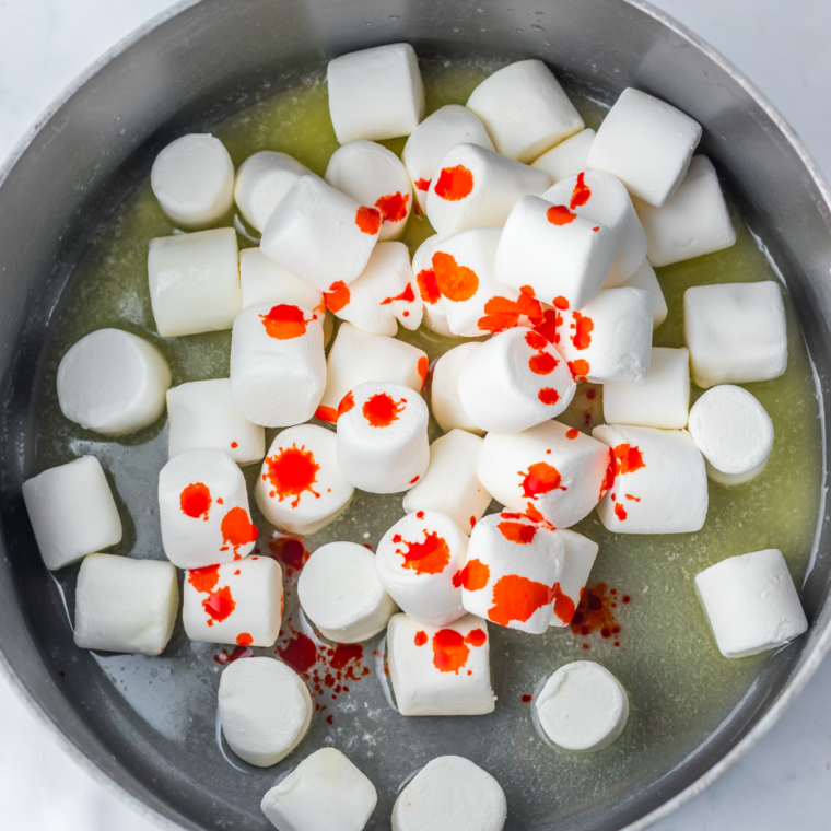Butter and marshmallows melting in a large pot with orange food coloring being stirred in