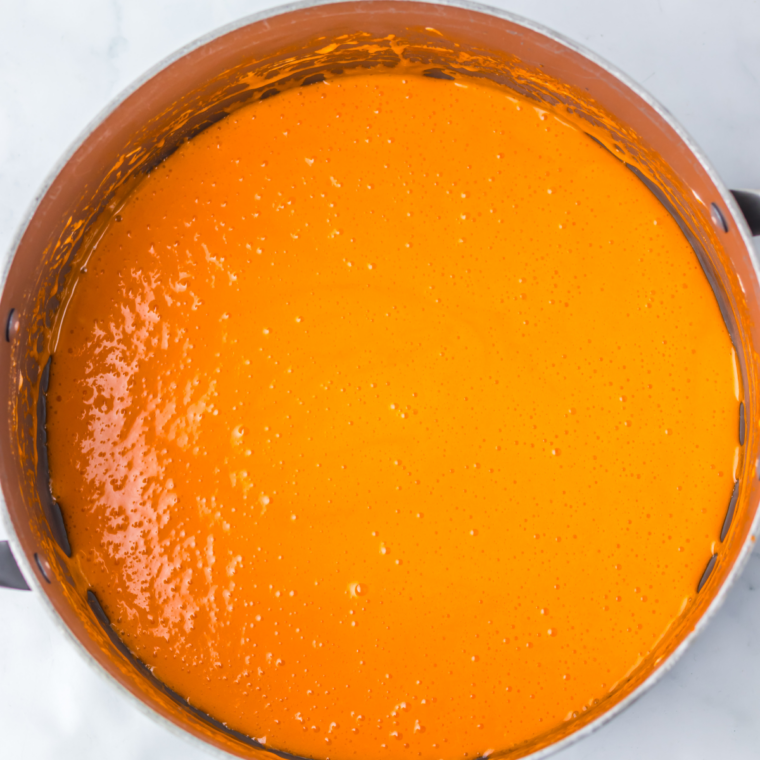 Melted marshmallow mixture tinted deep pumpkin orange in a pot with a wooden spoon