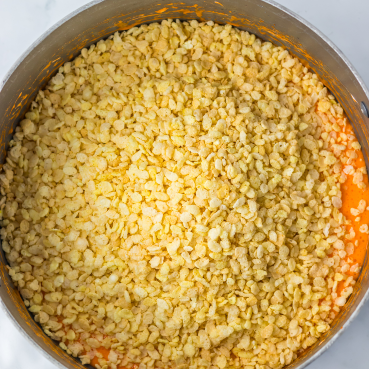 Rice Krispies cereal being stirred into orange melted marshmallow in a large pot