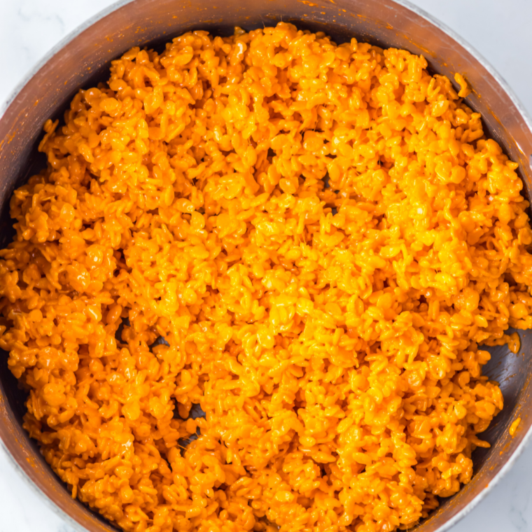 Orange marshmallow mixture and Rice Krispies cereal being stirred together in a large mixing bowl