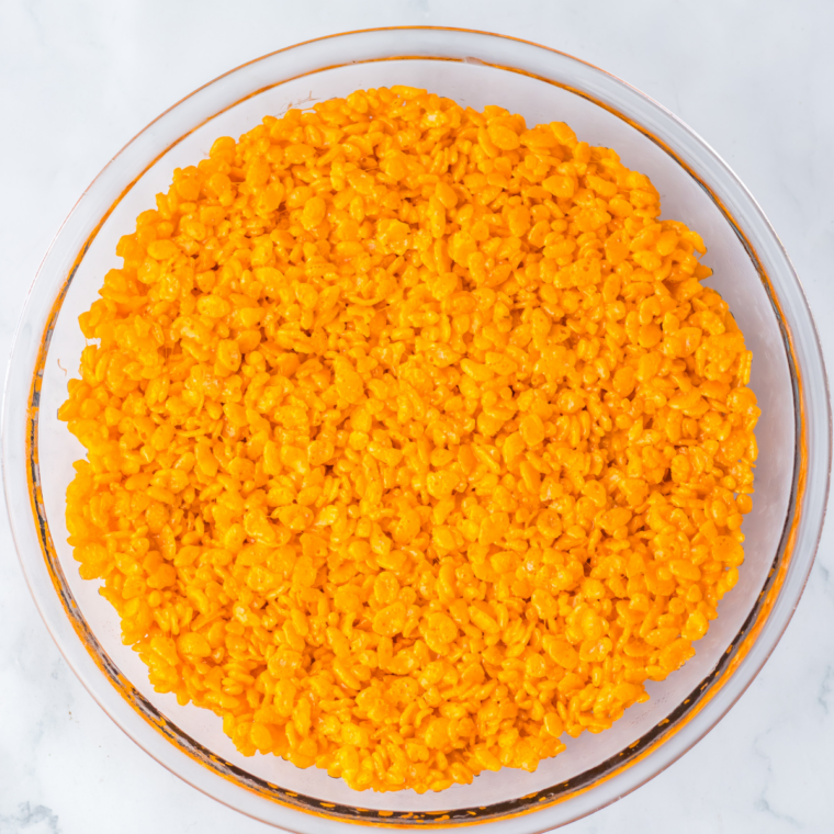 Orange Rice Krispie round releasing from an upside-down pie pan onto a lined baking sheet