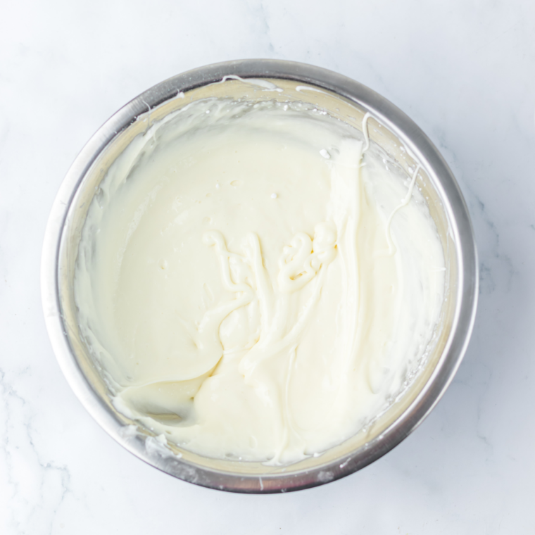 Cream cheese frosting beaten to a thick pipeable icing in a glass mixing bowl with a hand mixer