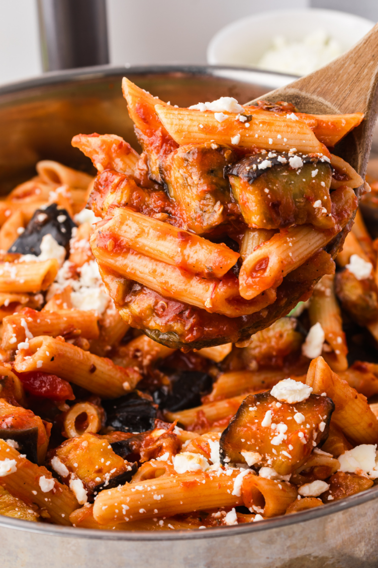 Bowl of spaghetti in roasted tomato pasta sauce beside a sheet pan of roasted tomatoes and garlic