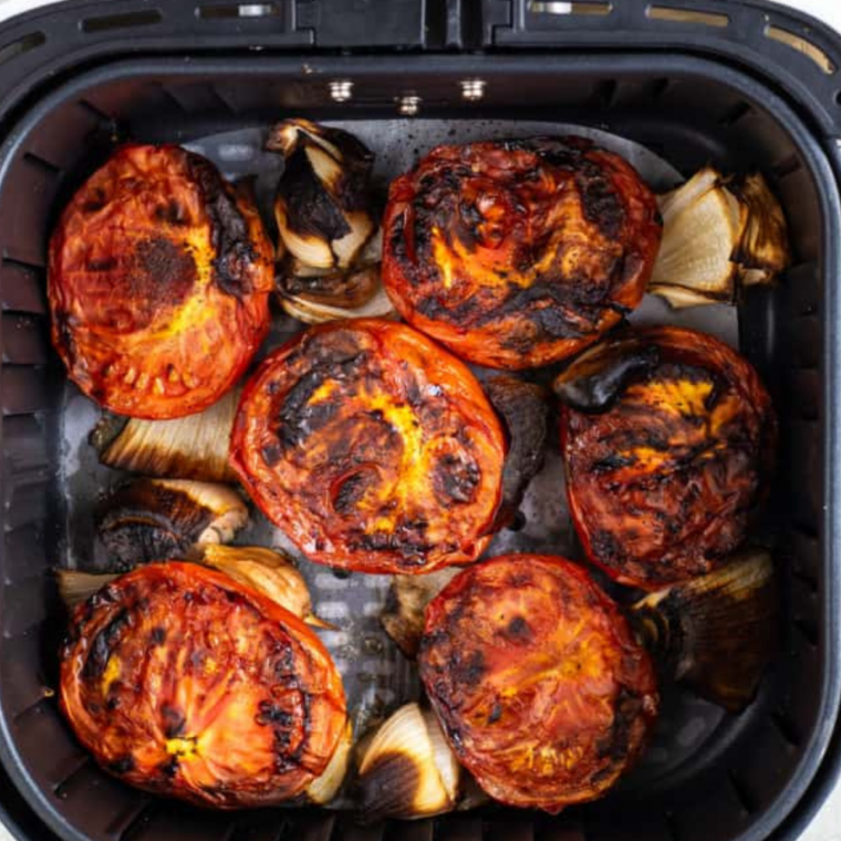 Roasted roma tomatoes with browned, wrinkled skins and charred onion edges in an air fryer basket