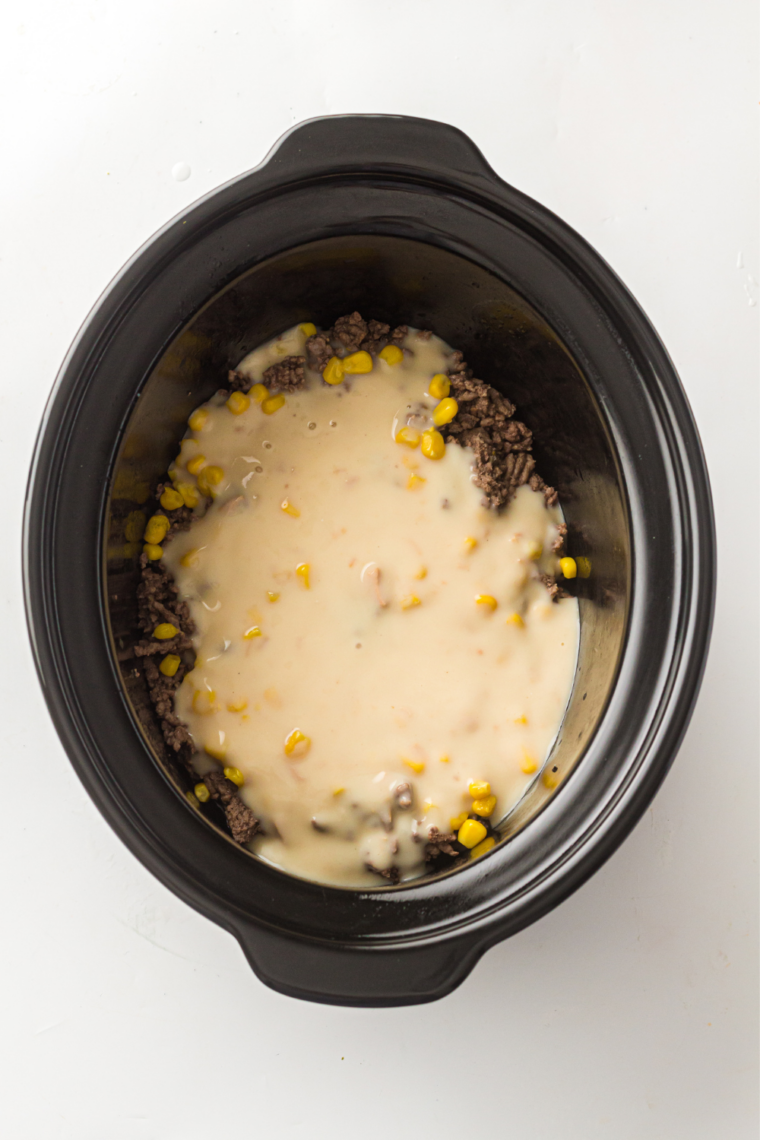 Cowboy casserole filling with ground beef, corn, cheese, and creamy soup mixed in a slow cooker