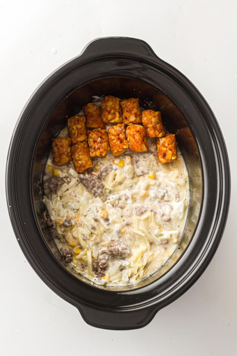 Frozen tater tots arranged in a single layer over the beef mixture in a slow cooker