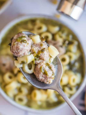 Slow cooker Italian wedding soup in a white bowl with chicken meatballs, orzo, spinach, and grated Parmesan