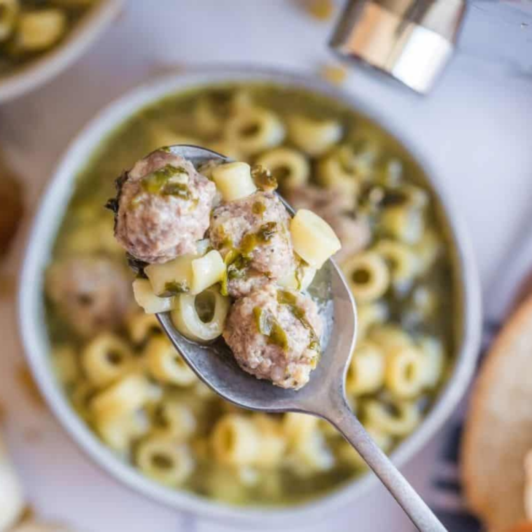 Slow cooker Italian wedding soup in a white bowl with chicken meatballs, orzo, spinach, and grated Parmesan