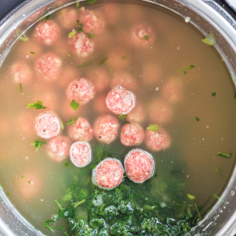 Browned meatballs and vegetables in a slow cooker with chicken stock and bay leaves