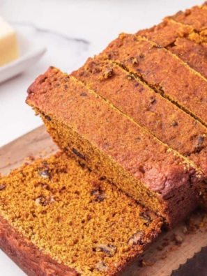 Slow cooker pumpkin bread sliced on a board with cinnamon sticks and a small pumpkin