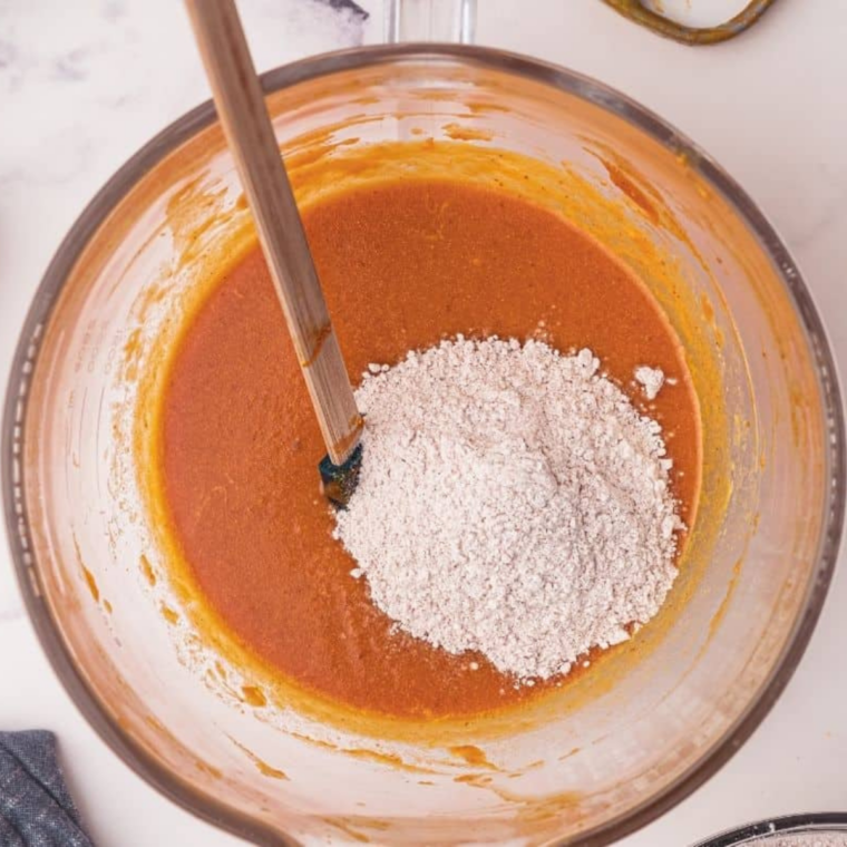 Adding flour to pumpkin bread batter in a mixing bowl