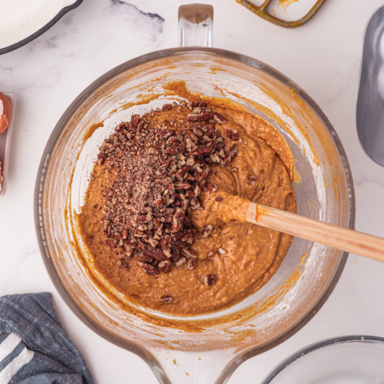 Adding chopped pecans to pumpkin bread batter in a mixing bowl