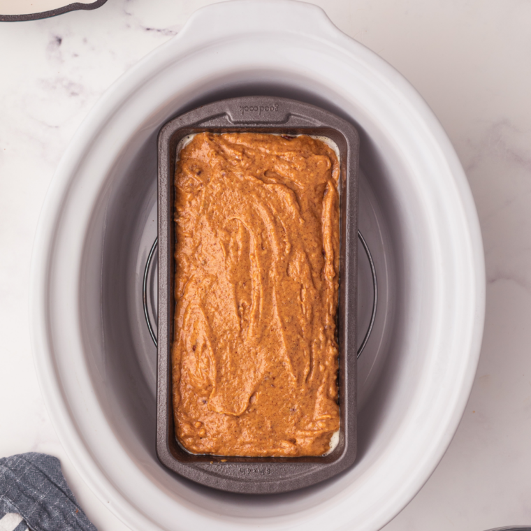Loaf pan of pumpkin bread batter set on a foil trivet inside a slow cooker