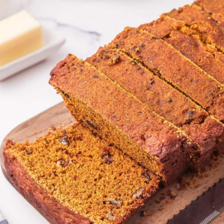 Slow cooker pumpkin bread sliced on a board with cinnamon sticks and a small pumpkin