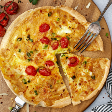 Air fryer egg tortilla frittata on a wooden cutting board with a fork, sliced into wedges