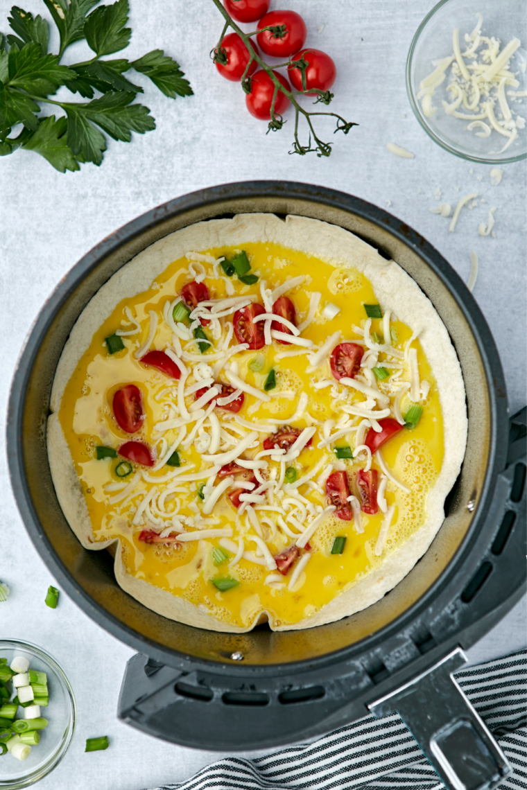 Whisked eggs with shredded cheese, bell pepper, and onion stirred into a glass mixing bowl