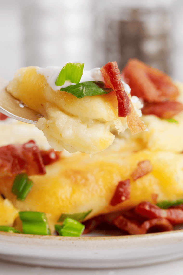 Fork lifting a serving of Chili's loaded mashed potatoes with melted cheese and bacon