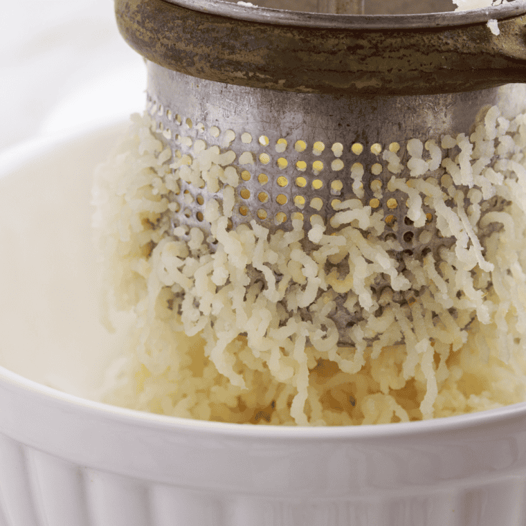 Potato masher pressing into skin-on potatoes with visible chunks and skin flecks