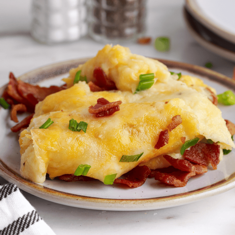 Chili's loaded mashed potatoes copycat in a white baking dish topped with melted cheddar jack cheese, crumbled bacon, and sliced chives