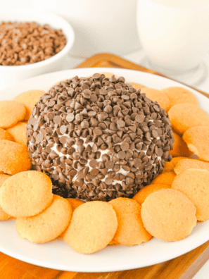 Chocolate chip cheese ball coated in mini chocolate chips on a white platter with graham crackers and pretzels
